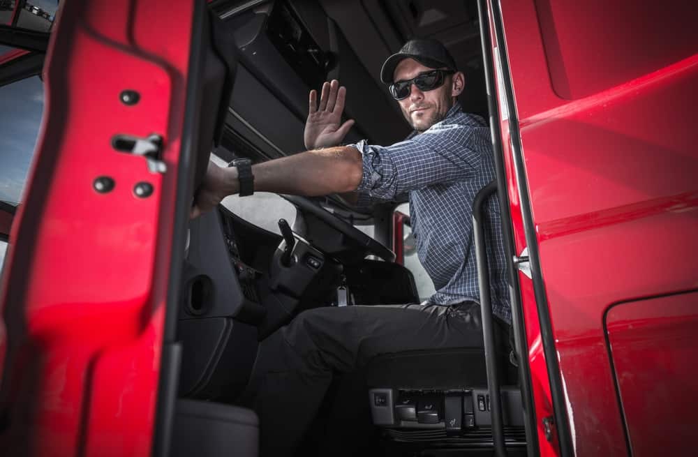 Truck driver inside red truck waving at camera