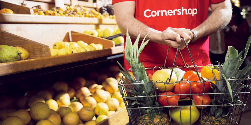 Cornershop worker holds basket of fresh fruits and vegetables in the produce section of a grocery store.