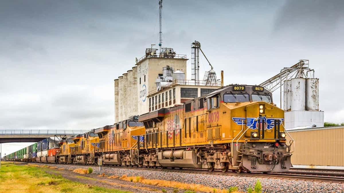 A photograph of a train in front of a grain elevator.