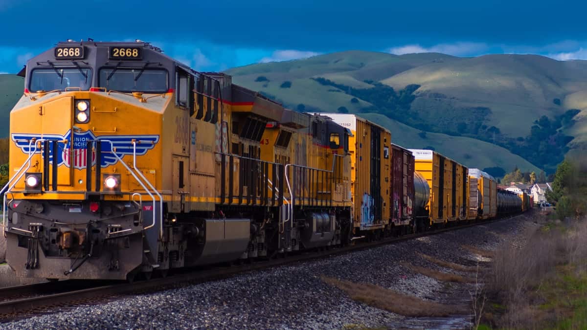 A train travels on train tracks. Behind the train are mountains.