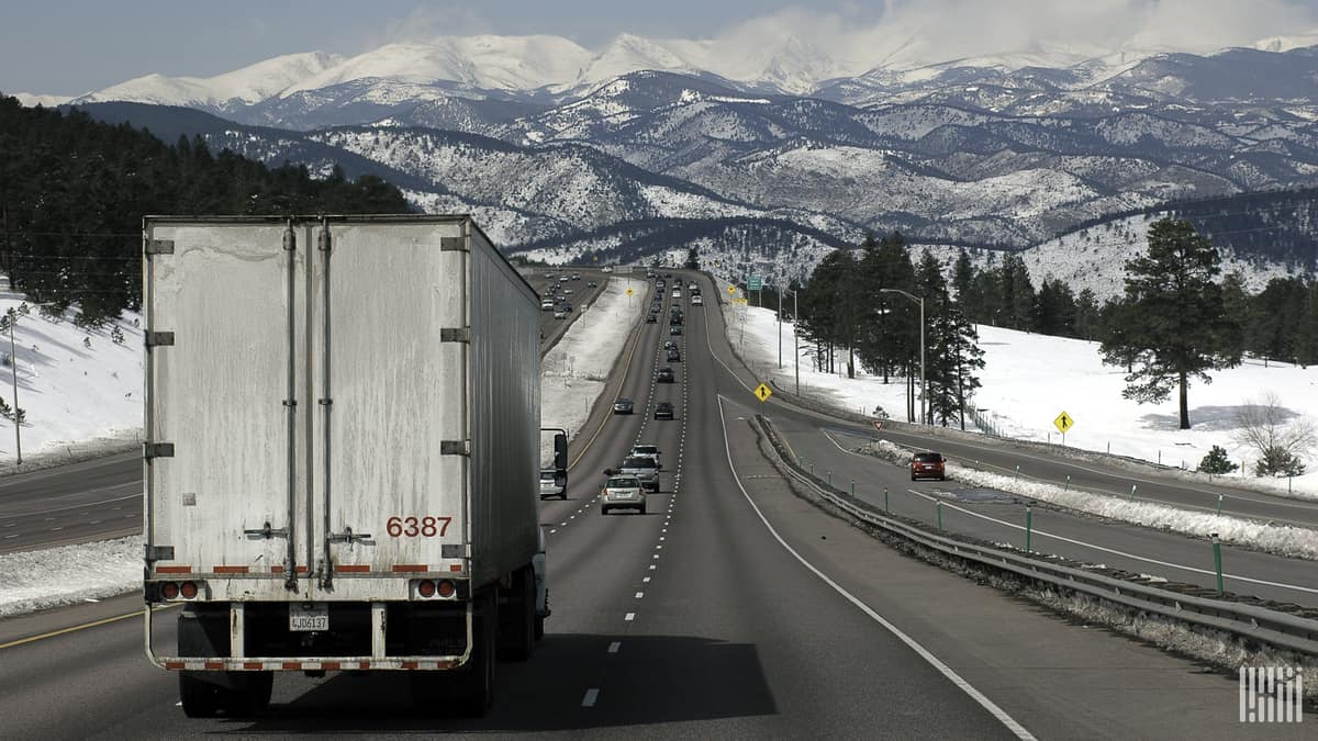 Tractor-trailer on I-70 in Colorado, surrounded by snow-covered mountains and grass.