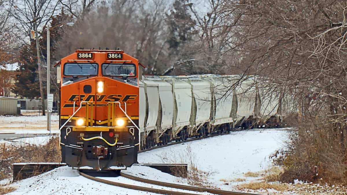 A photograph of a train passing through patches of snowy ground.