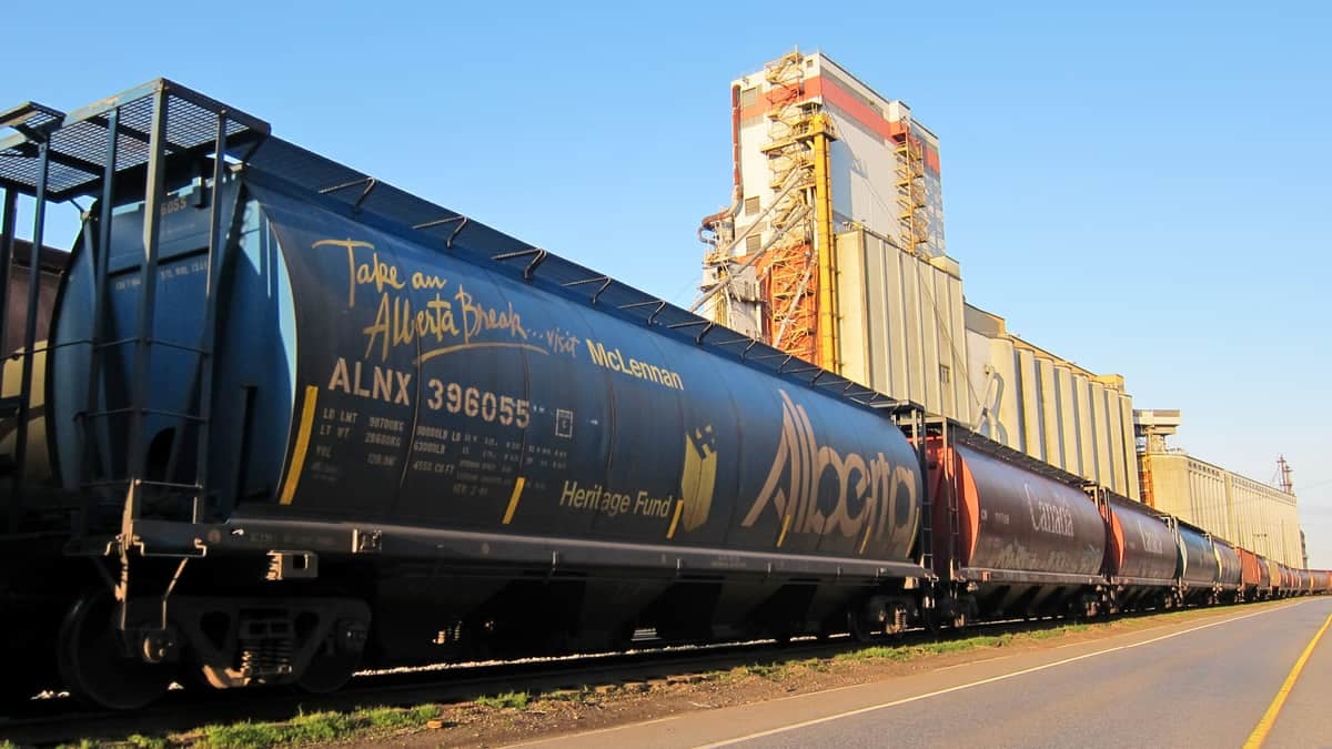 A photograph of a tank car and some railcars at a grain elevator.