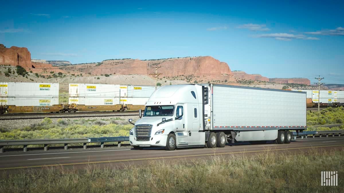 A photograph of a truck. Intermodal containers are behind the truck.