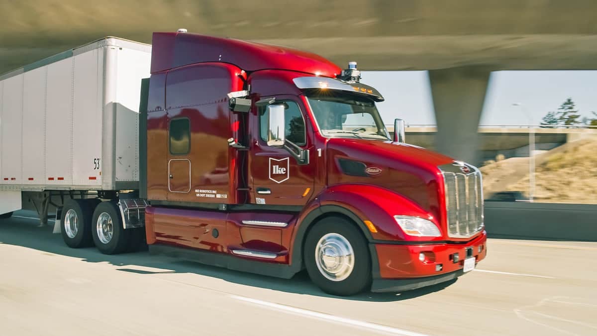 A photograph of a truck pulling a trailer. The truck is on the road and in front of a bridge.