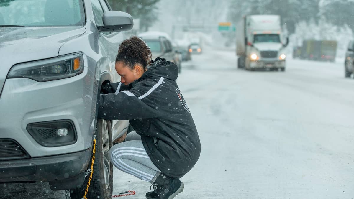 Driver putting chains on her tires on snowy Oregon road.