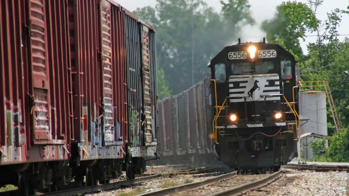 A photograph of a locomotive pulling boxcars. Some parked boxcars are next to the locomotive.