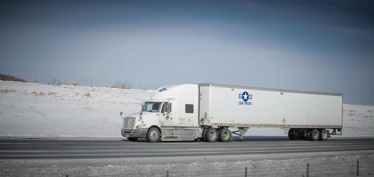 Tractor-trailer on a road with snow on the grass in background.