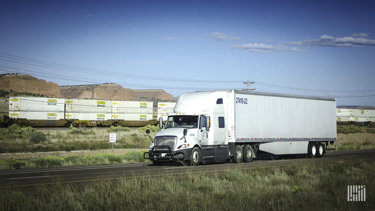 White truck with double-stack intermodal train in background