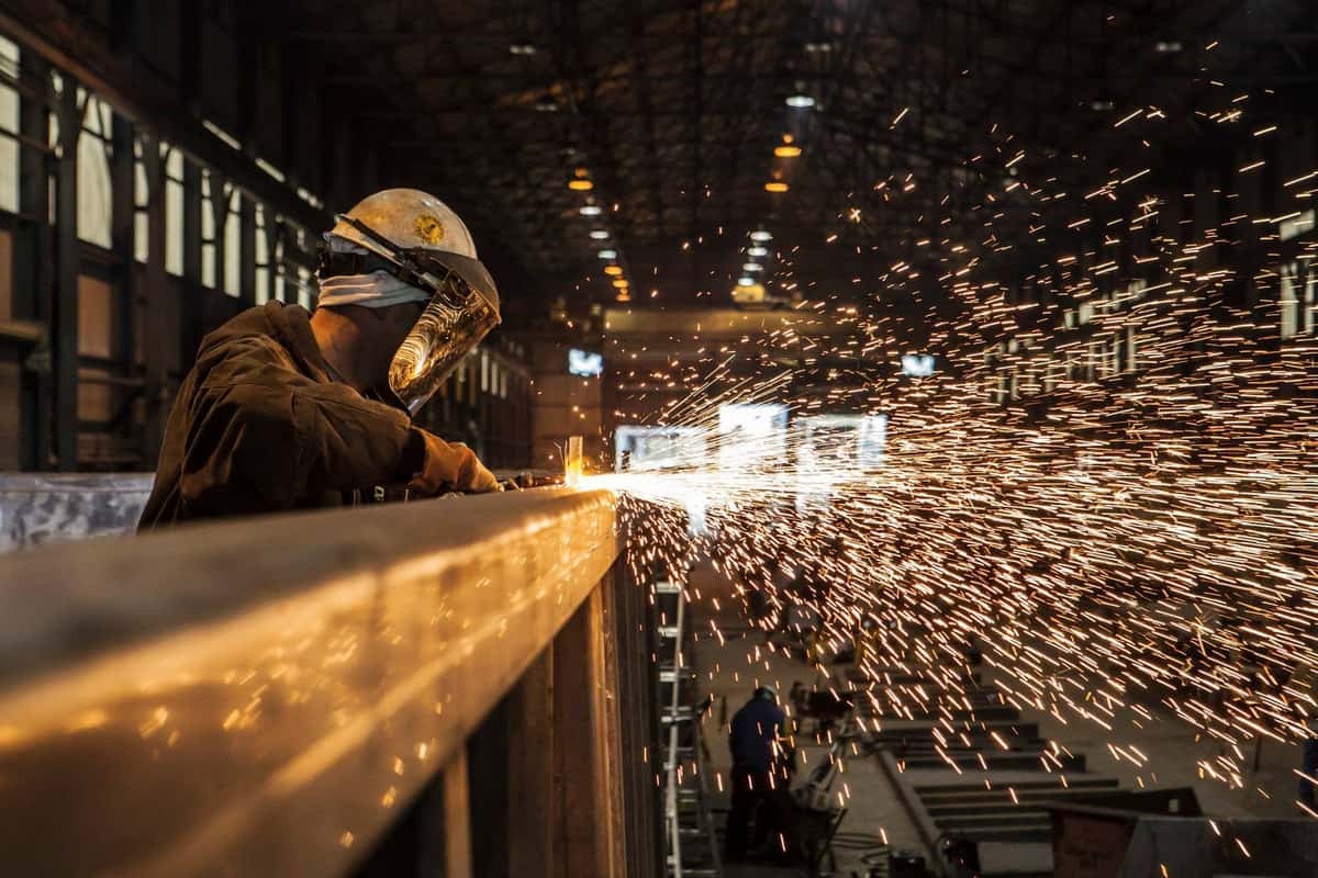 A photograph of a worker melding equipment. Sparks of fire are coming from the equipment.