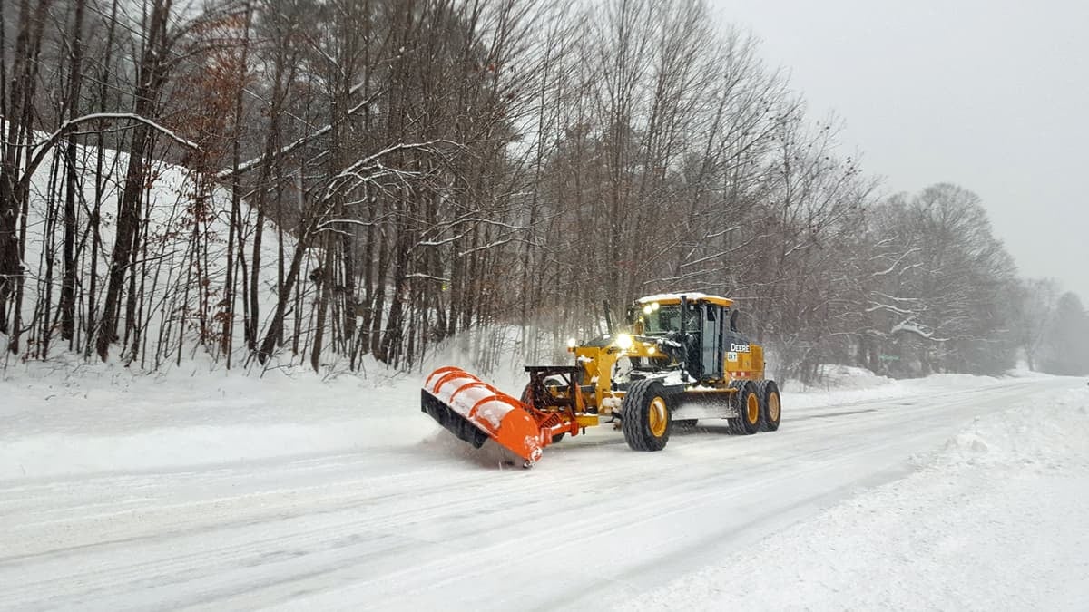 Plow clearing snowy New Hampshire road.