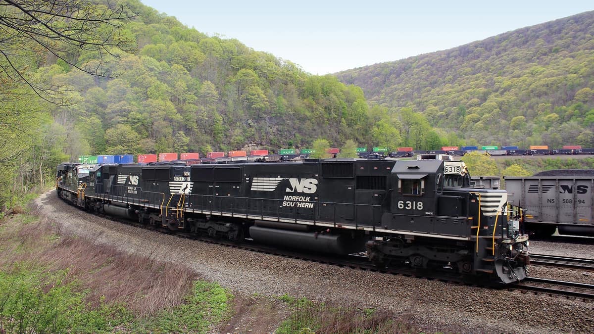 A photograph of a train locomotive hauling intermodal containers by two hillsides.