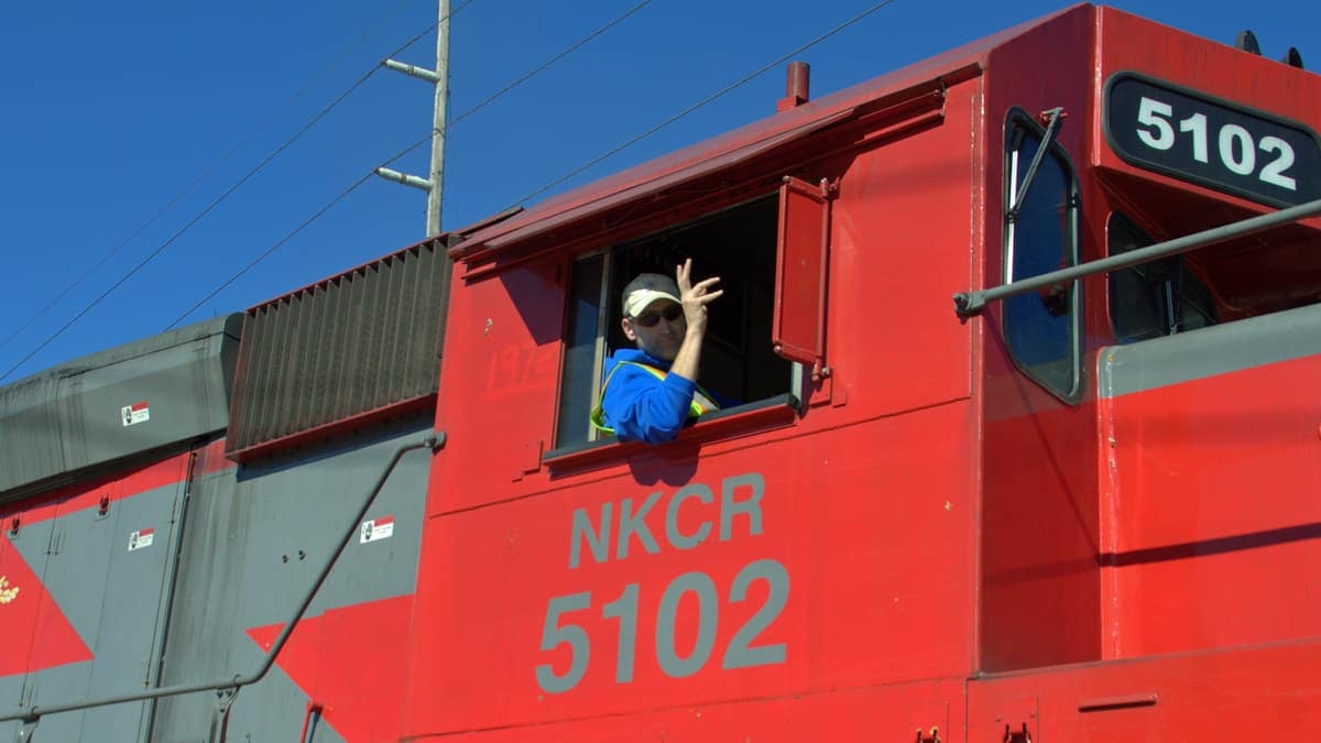 A photograph of a man leaning out of the window of a train.