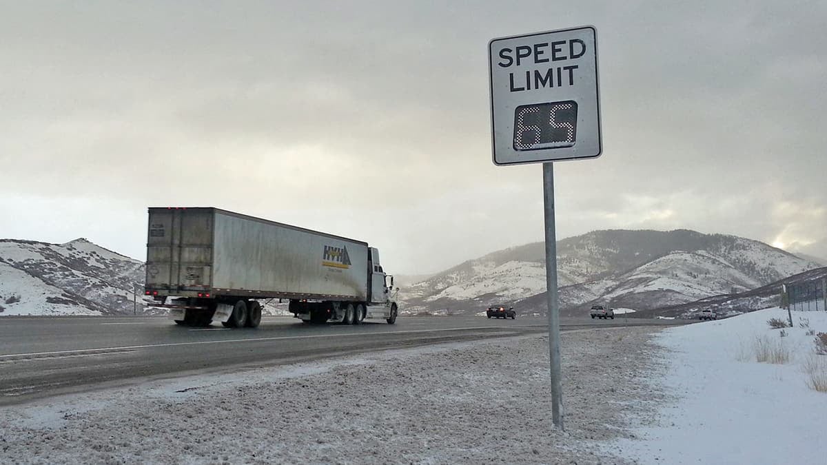 Tractor-trailer on Utah highway surrounded by snow-capped mountains.