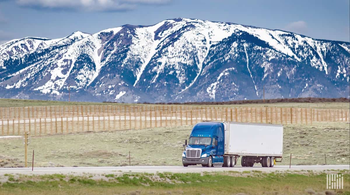 unidentified tractor-trailer on highway with snowy mountains in backdrop