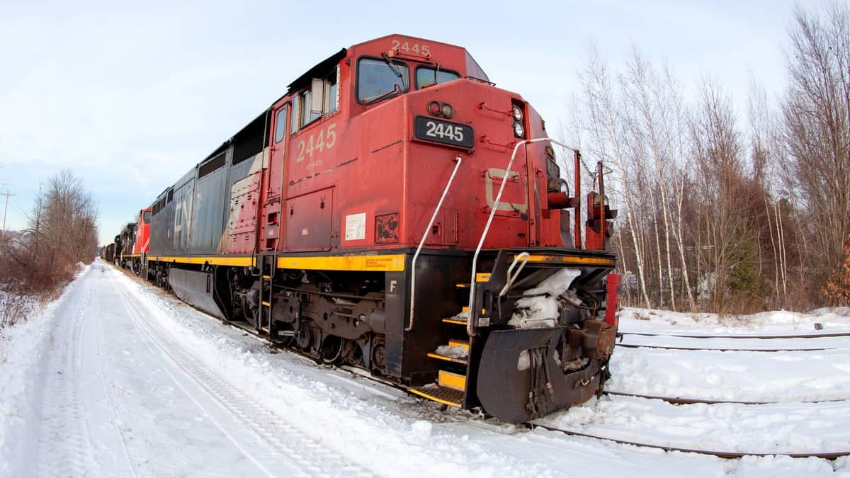 A photograph of a train. There is snow on the ground and bare trees next to the train.