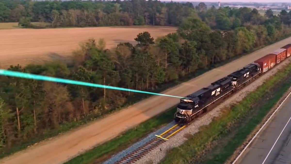 An image of a locomotive hauling railcars through a field. The locomotive has a laser beam coming out of its top. The laser beam is pointing outward and to the left.