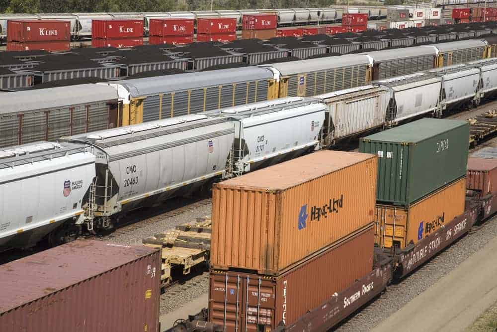 A photograph of different types of railcars sitting on rail tracks at a rail yard.