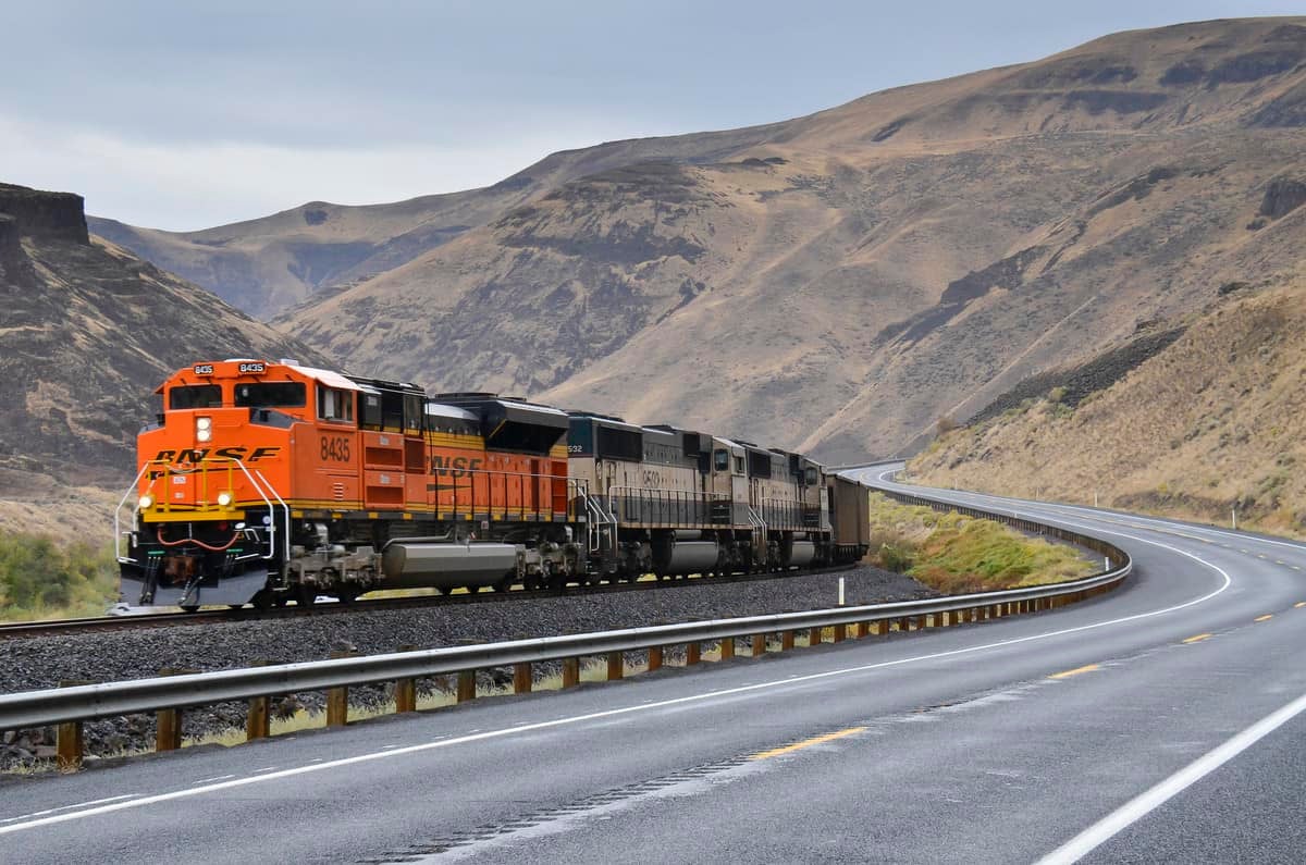 A photograph of a train. There is a road next to the train, and there are two hills behind the train.