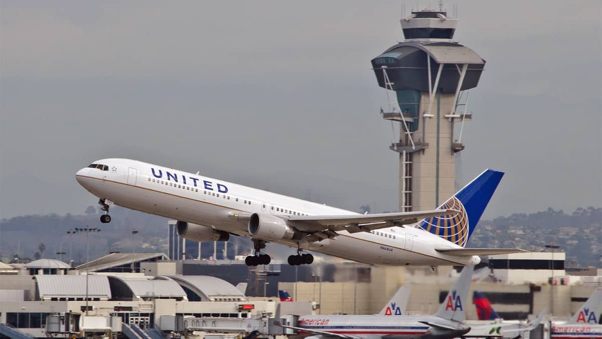 A white United plane takes off with control tower in background.