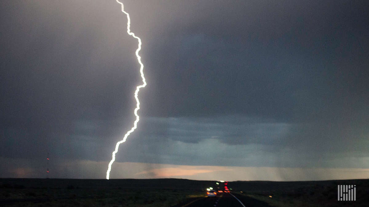 Tractor-trailer heading down highway with lightning across the shy.