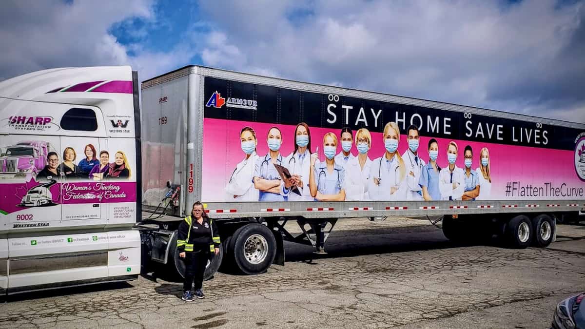 Shelley Uvanile-Hesch standing in front of her tractor-trailer, wrapped with the message "Stay Home. Save Lives"