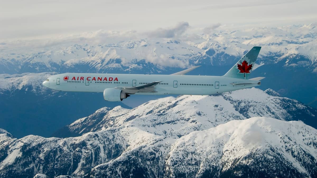 Big white plane flies high over snow-capped mountains.