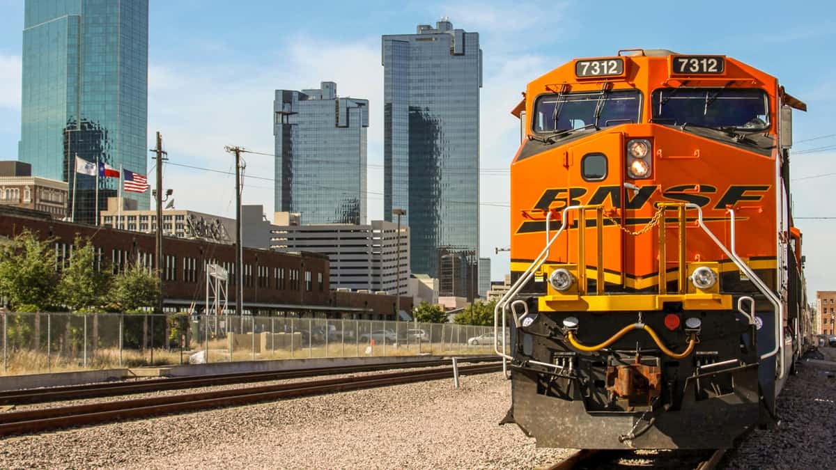 A photograph of a train locomotive on a train track. Behind it are skyscraper buildings.