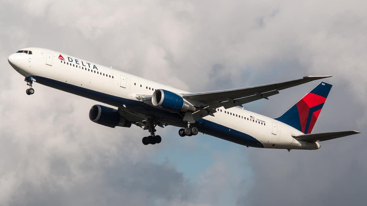 A big white Delta plane takes off in cloudy sky.