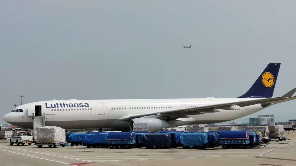 A big white jet with blue tail surrounded by cargo carts on the ground.