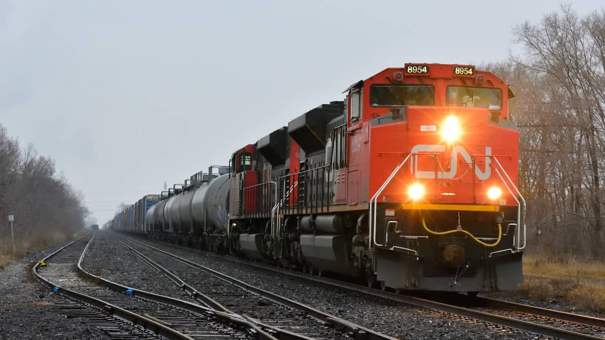 A photograph of a locomotive engine hauling railcars. Trees line either side of the track.