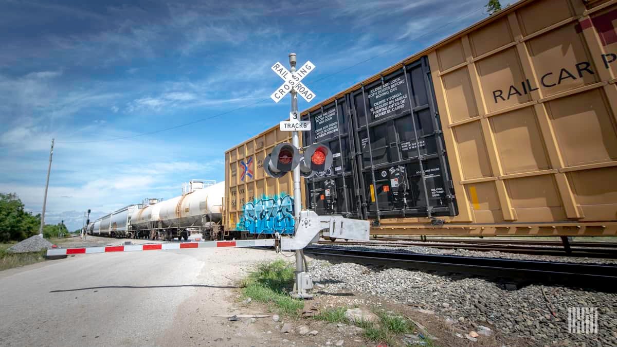 A photograph of boxcars and tank cars at a rail crossing.