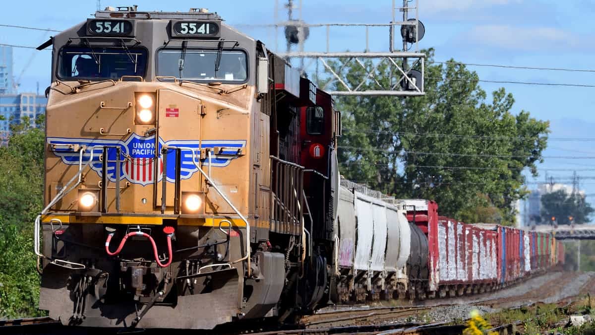 A photograph of a train locomotive pulling railcars on a sunny day.