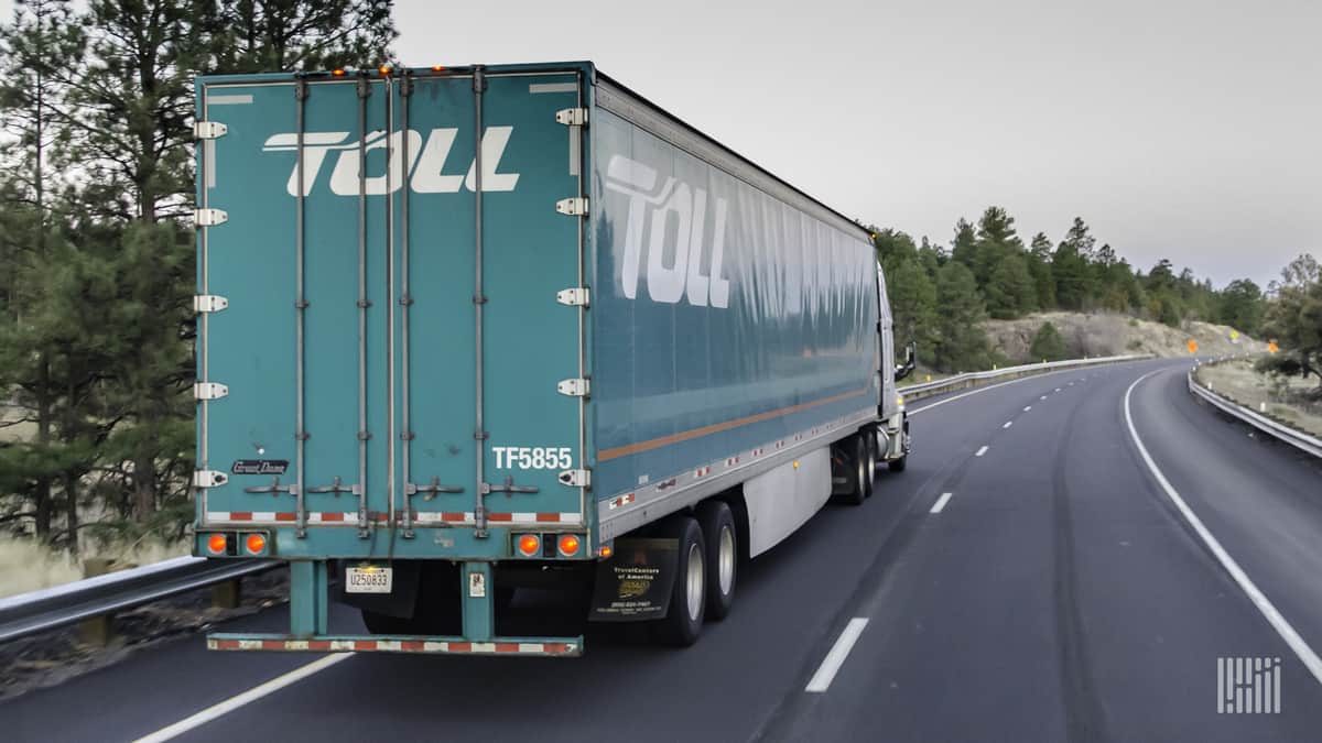 Green truck driving on highway, view from behind.