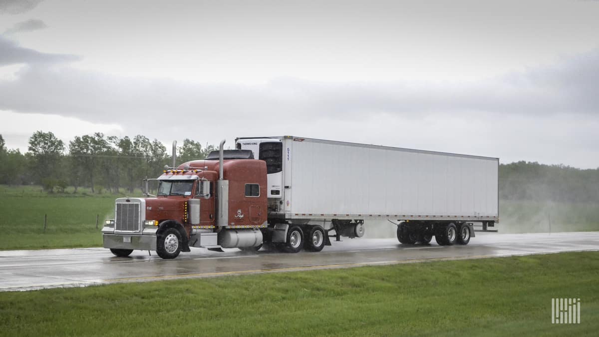 Tractor-trailer on wet highway with storm cloud in the background.