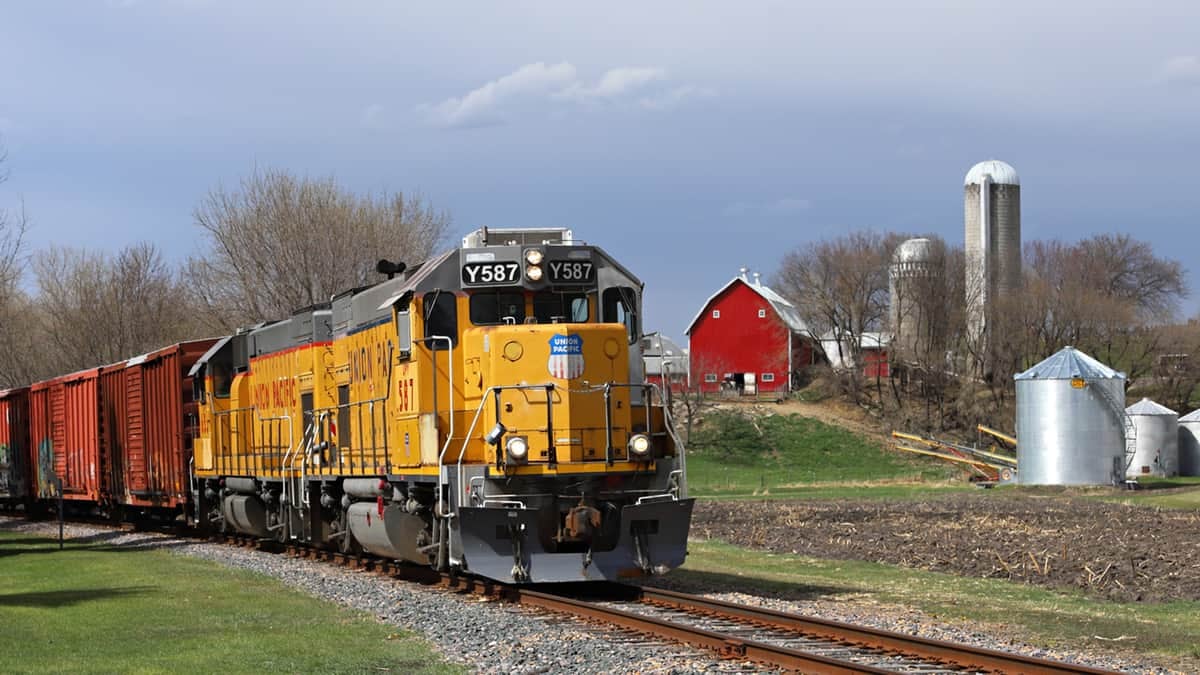 A photograph of a train traveling past a farm.