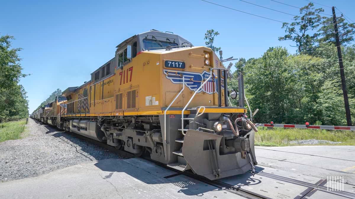 A photograph of a train locomotive on a train track. There is a forest next to the train track.