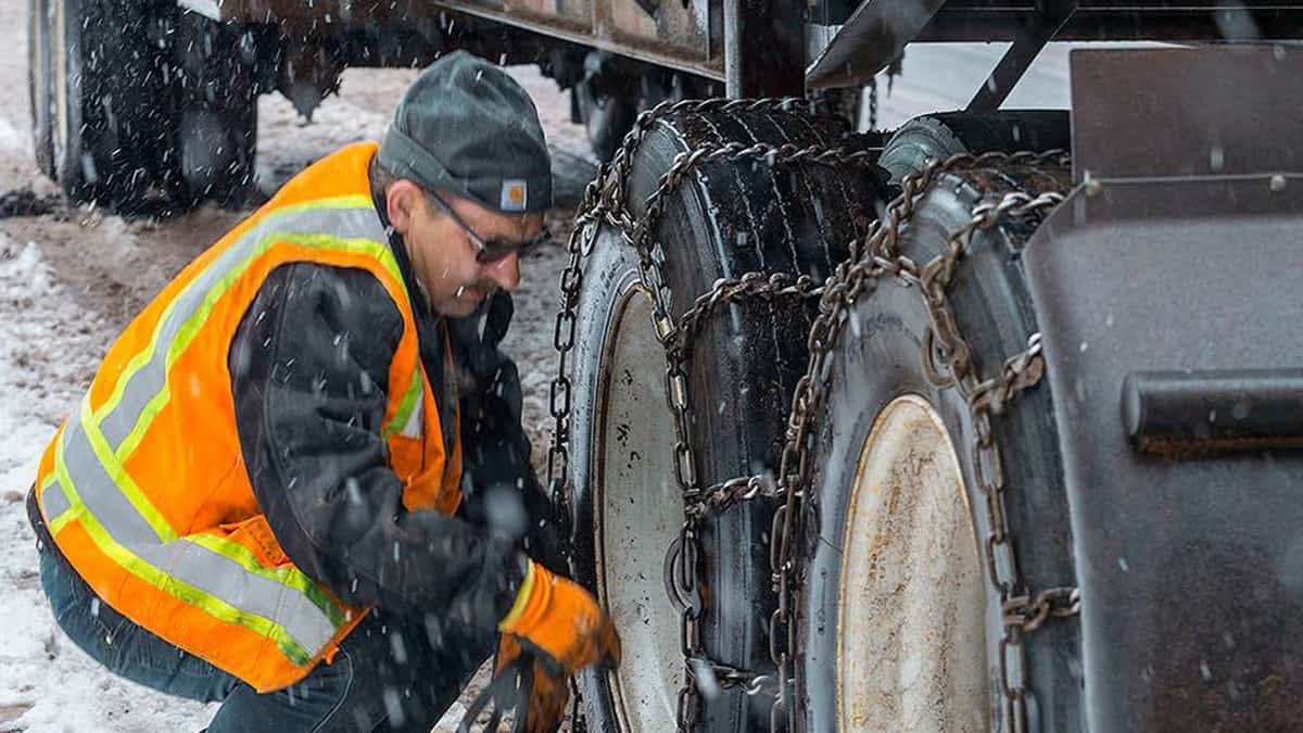 Truck driver putting chains on his tires in the snow.