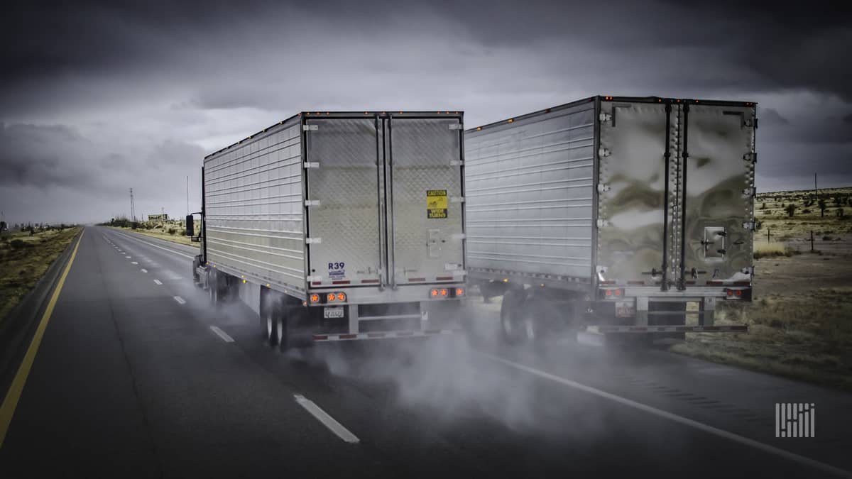 Tractor-trailers heading down wet highway surrounded by dark skies.