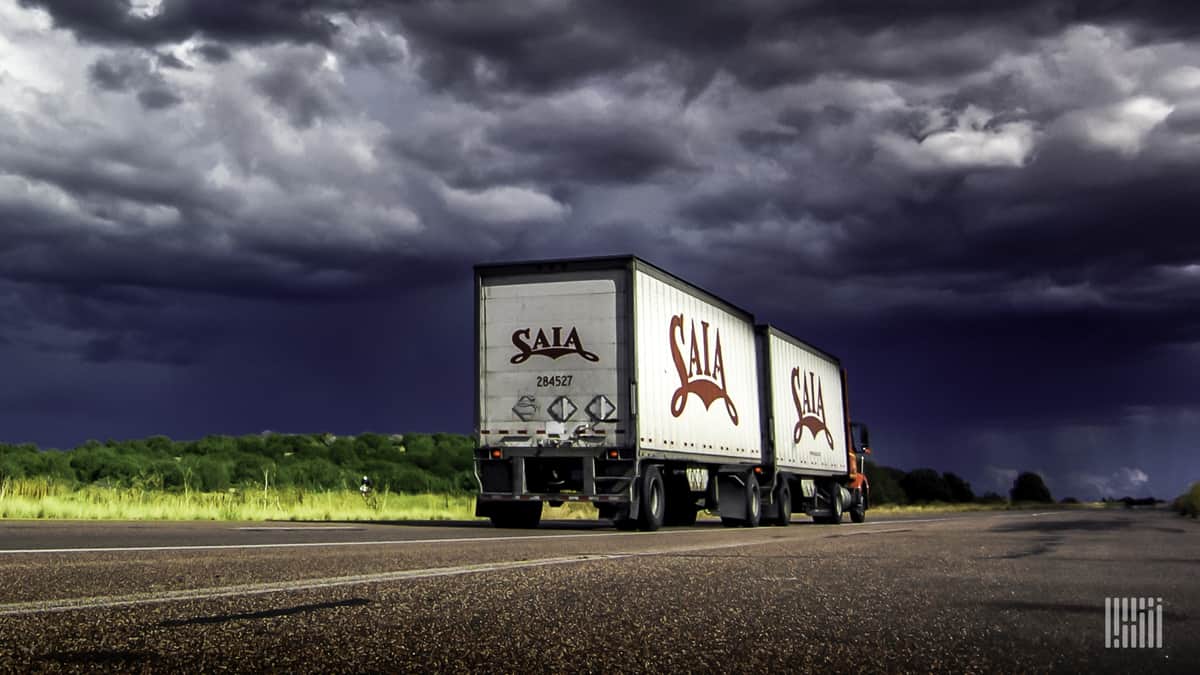 Tractor-trailer heading down highway, with thunderstorm ahead.