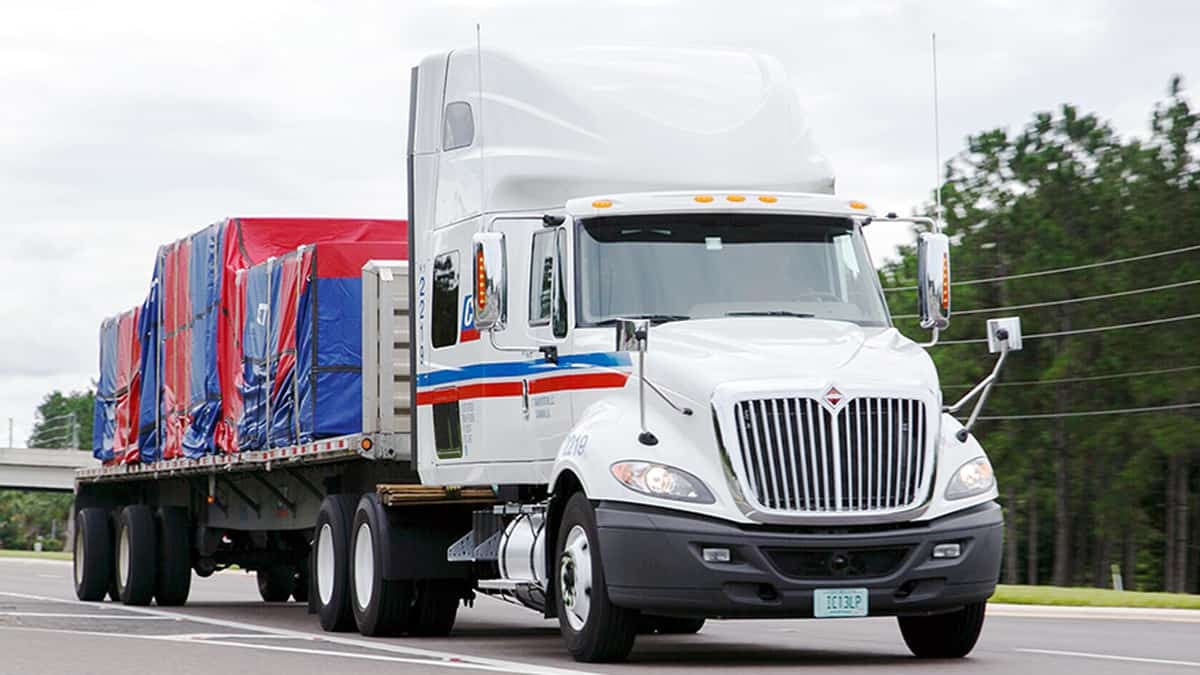 A tractor-trailer of CT Transportation hauls a flatbed load. TFI International acquired nearly all of CT assets from Comcar.