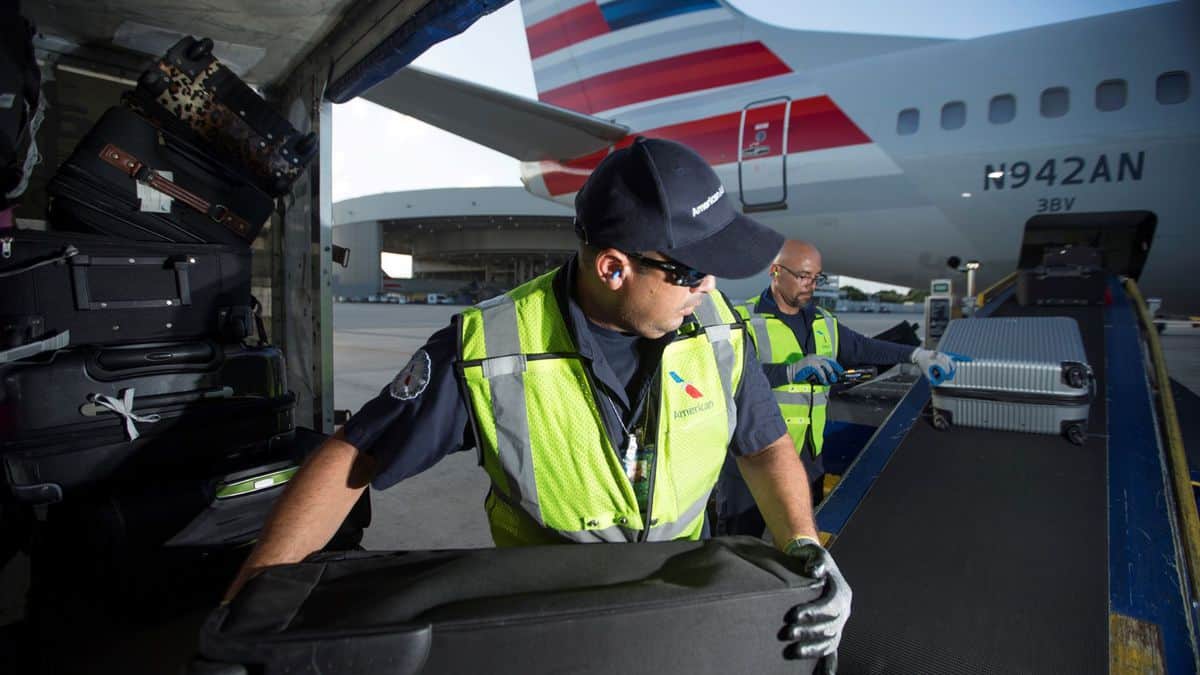 A baggage worker transfers bags from a cart to a conveyor belt for loading onto a plane. Ground workers at American Airlines are among thousands of employees who could lose their jobs.