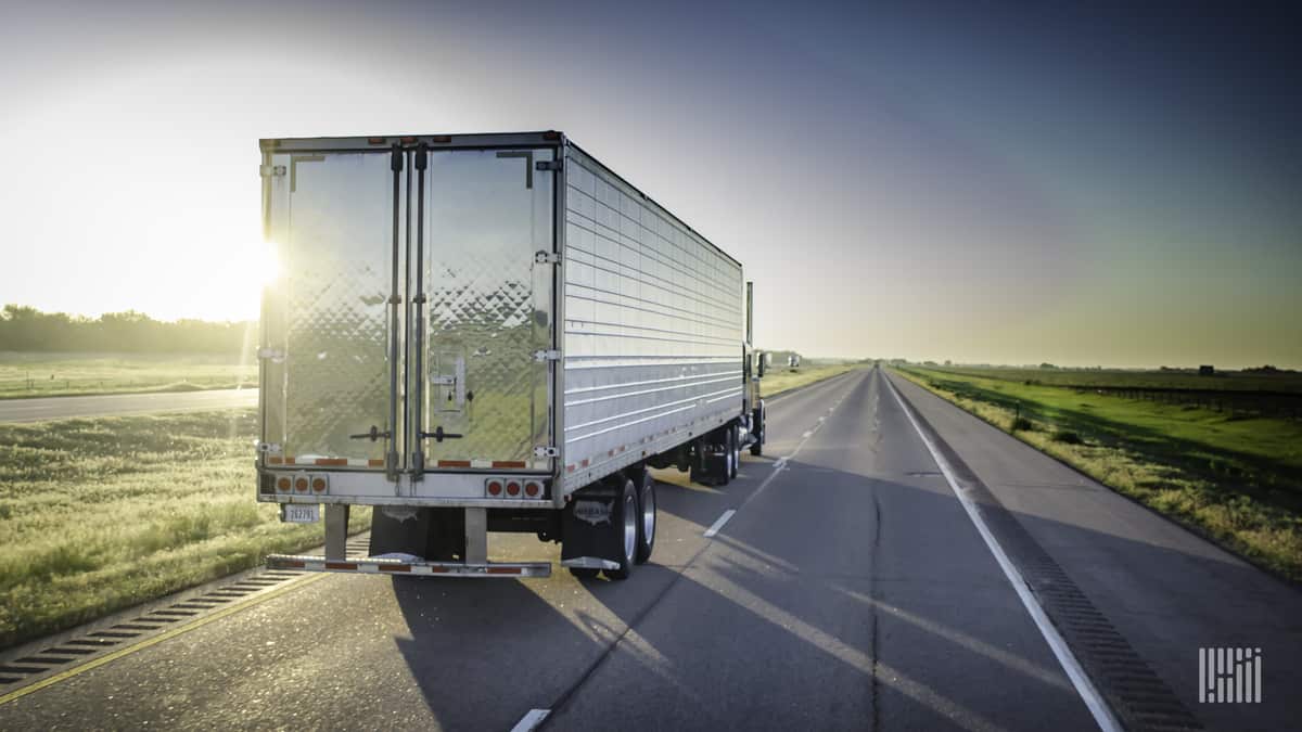 Tractor-trailer heading down desert highway with bright sunshine across the sky.