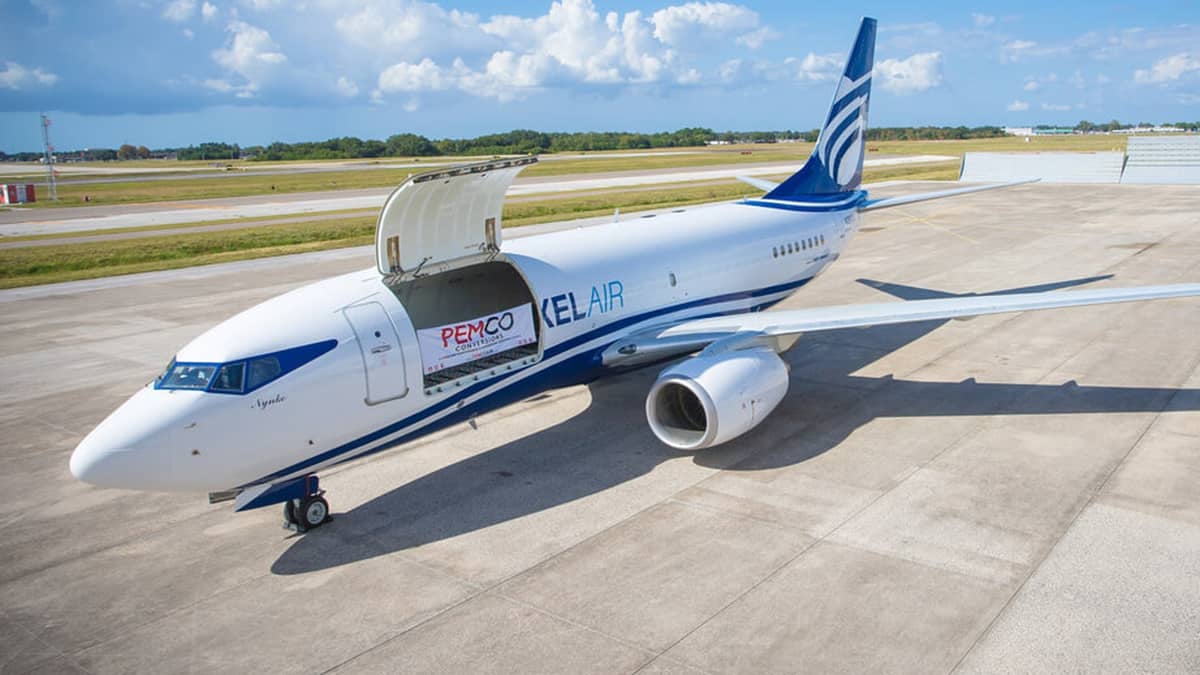 A white Boeing 737 with blue tail sitting on tarmac on bright sunny day with big cargo door open. Pemco is converting these planes into freighters.