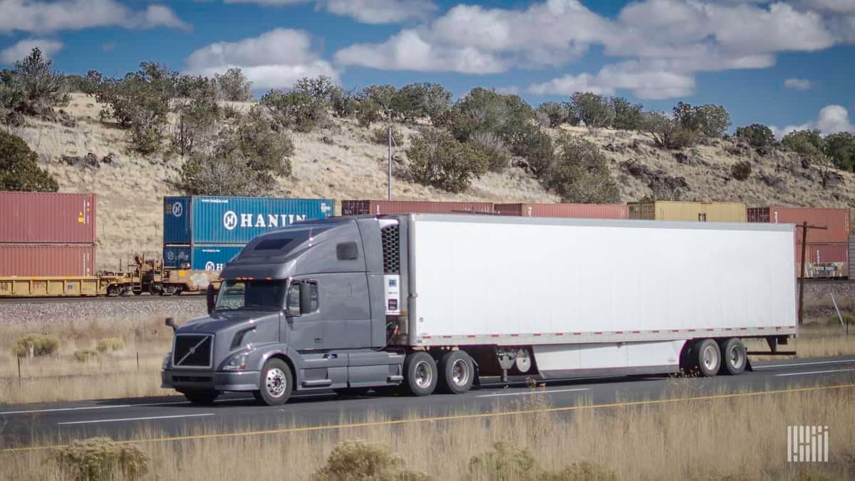 A photograph of a truck with a trailer and an intermodal train behind the truck.