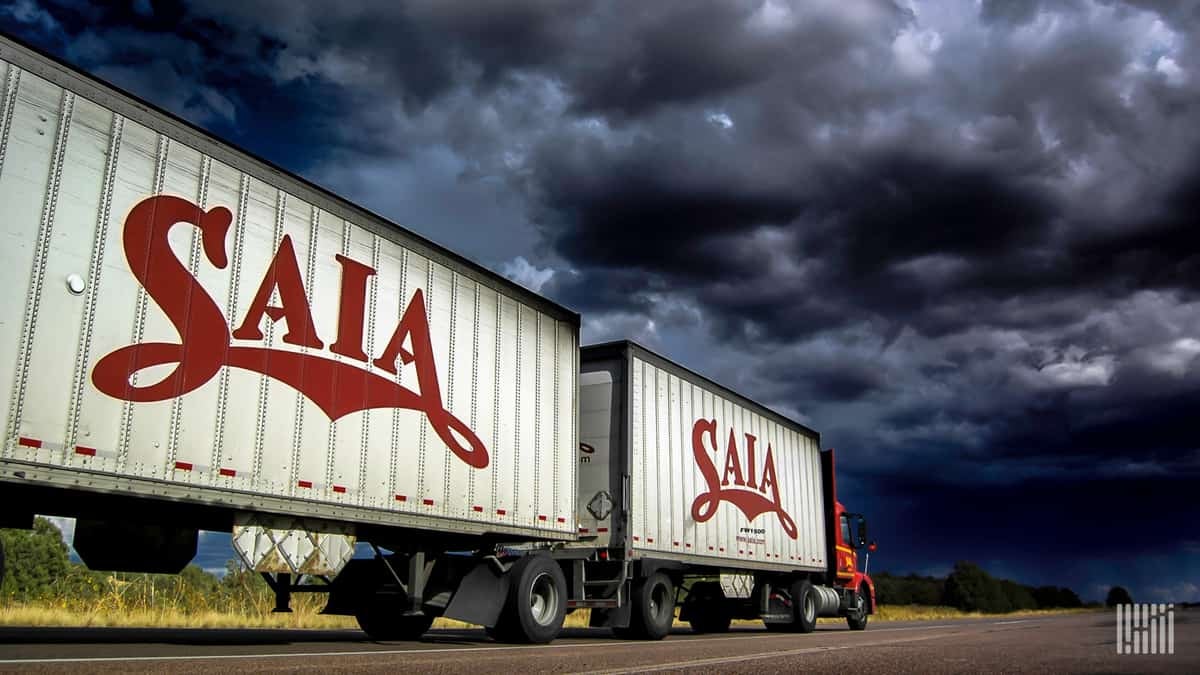 SAIA tractor-trailer heading down highway with dark storm cloud across the sky.