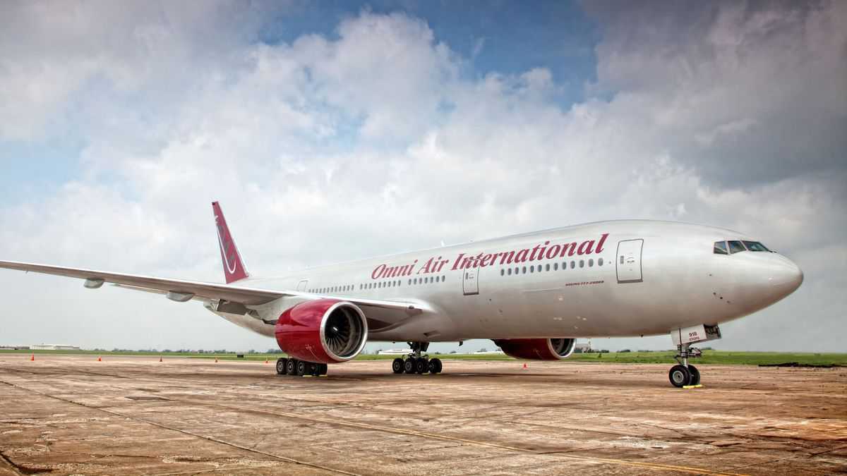 A white Omni Air passenger jet sits on tarmac under gray sky.