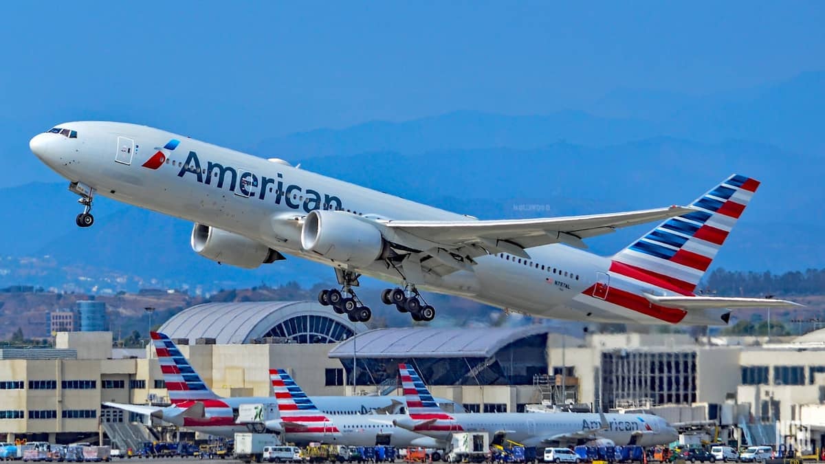 A big silver American Airlines jet takes off with bright blue sky, airport in background. American is flying more cargo-only flights.