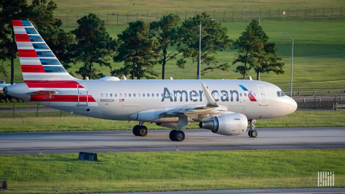 A silver American Airlines plane with red, white and blue striped tail rolls down taxiway. American plans to cut 19,000 jobs.