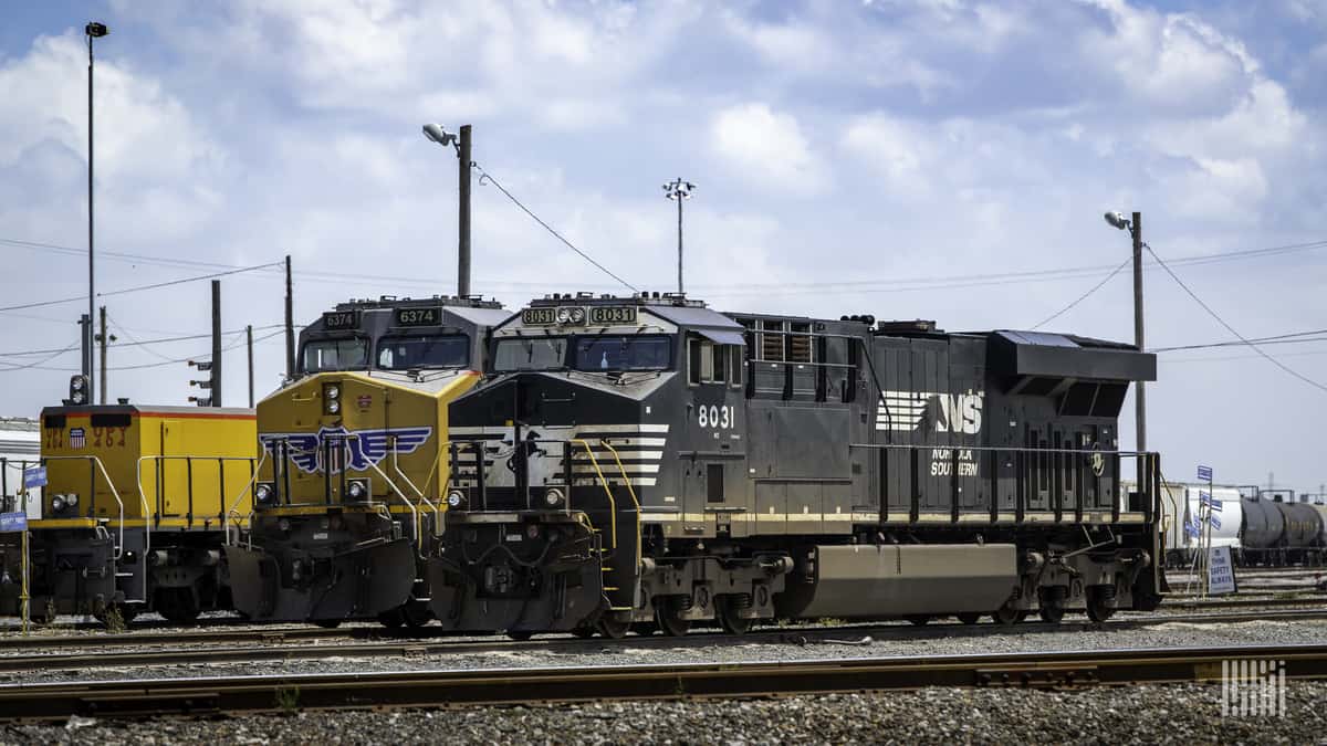 A photograph of a Norfolk Southern locomotive and another freight train locomotive parked at a rail yard.